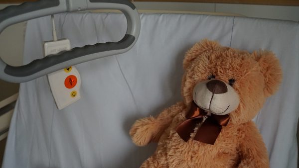 Zu sehen ist ein Teddy auf einem Krankenbett